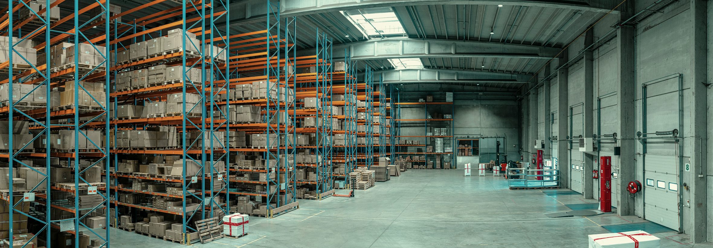 Interior de um centro de distribuição com porta-pallets carregados e área de expedição